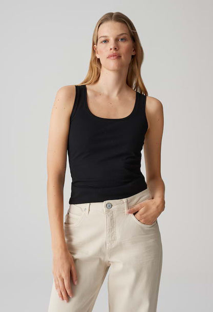 Woman wearing a black tank top and light-colored pants against a plain background