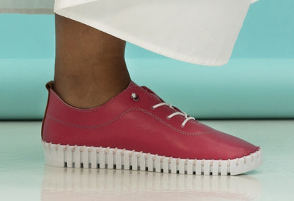 A pair of pink leather Plimsoll shoes with a lace-up closure, displayed on a person standing against a white background.