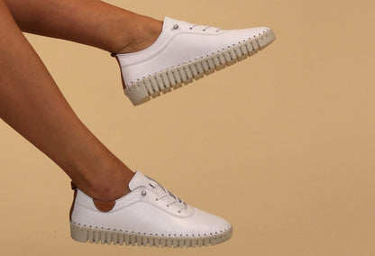 A pair of white leather Plimsoll shoes with a lace-up closure, displayed on a person standing against a white background.