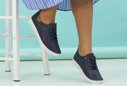 A pair of navy leather Plimsoll shoes with a lace-up closure, displayed on a person standing against a white background.