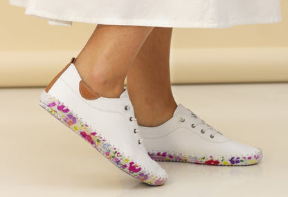 A person wearing white leather plimsolls with a floral print sole.