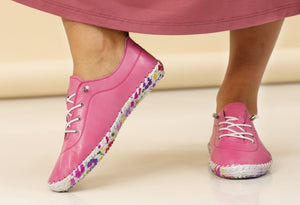 A person wearing pink leather plimsolls with a floral print sole.