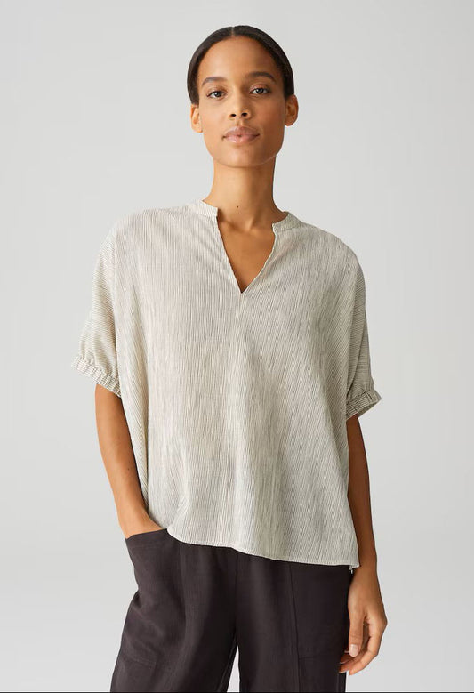 Woman wearing a light-colored blouse and dark pants against a plain background