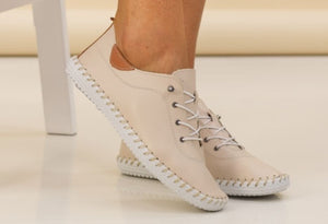 a lace up, leather plimsoll on a models foot on a beige background