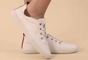 white leather plimsoll, lace up on a models foot on a beige background