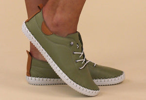 a khaki green leather plimsoll with laces, on a models foot on a beige background