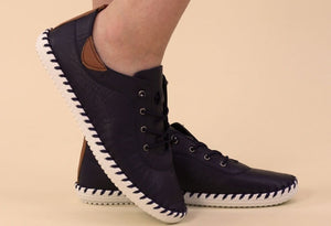 a navy leather plimsoll on a models foot on a beige background