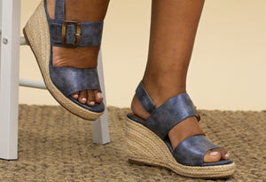 a pair of blue metallic wedges on a models foot with a beige background