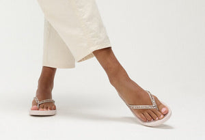 A pair of light pink, Fit Flop crystal-embellished toe-posts sandals on a model's feet against a white background.