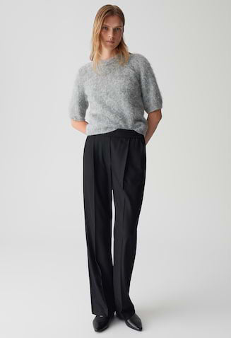 Person wearing a gray sweater and black pants on a white background