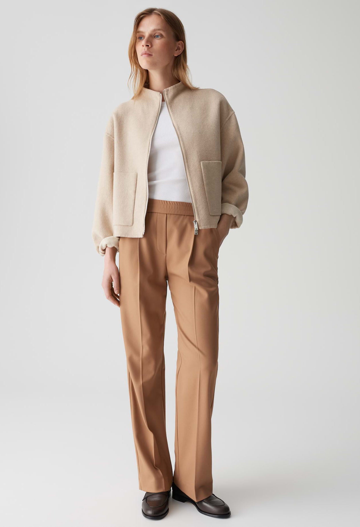 Woman wearing a beige jacket and brown pants on a white background