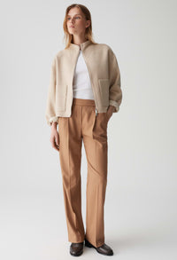 Woman wearing a beige jacket and brown pants on a white background