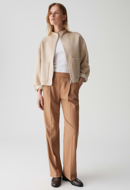 Woman wearing a beige jacket and brown pants on a white background