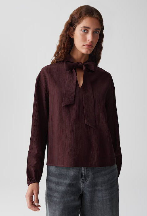 Woman wearing a dark brown blouse with a bow tie and jeans on a light gray background