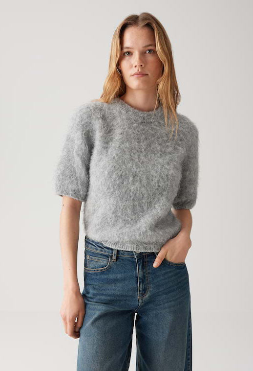 Woman wearing a gray sweater and blue jeans against a plain background