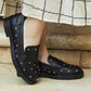 Black loafers with silver studs worn by a person on stone steps.