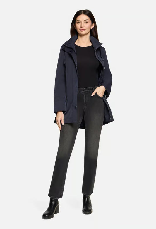 Woman wearing a navy coat, black top, and dark pants on a white background