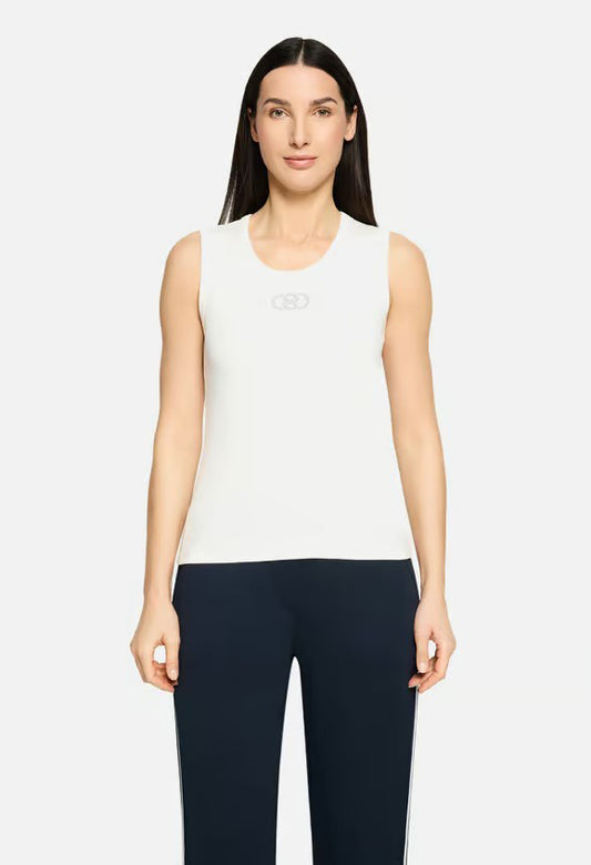 Woman wearing a white sleeveless top and dark pants on a white background