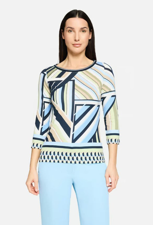 Woman wearing a patterned top and light blue pants on a white background