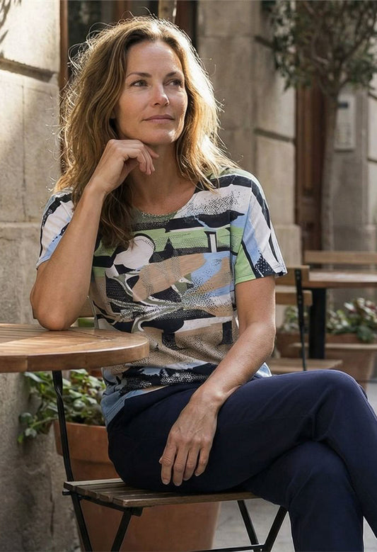 Woman sitting at an outdoor cafe table wearing a patterned shirt.