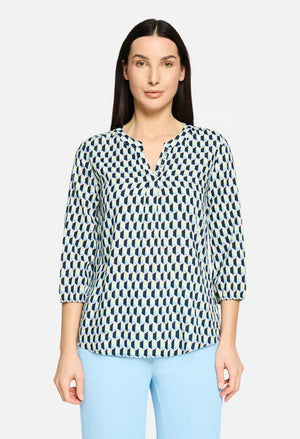 Woman wearing a patterned blouse and light blue pants on a white background