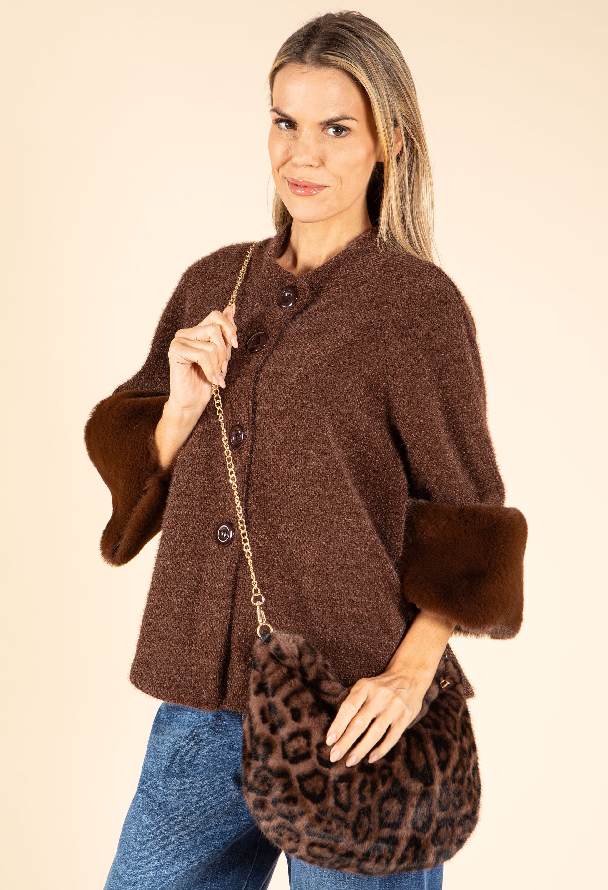Woman wearing a brown coat with fur cuffs holding a leopard print bag on a beige background