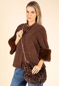 Woman wearing a brown coat with fur cuffs holding a leopard print bag on a beige background