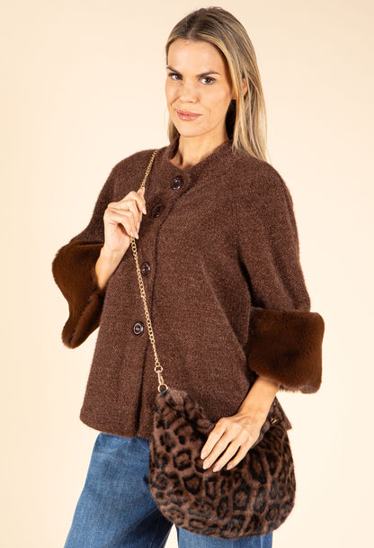 Woman wearing a brown coat with fur cuffs holding a leopard print bag on a beige background