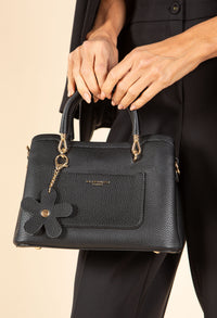 Black handbag with a decorative flower detail held by a person against a beige background