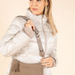 Woman wearing a white puffer jacket with a beige crossbody bag on a beige background