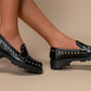Black loafers with stud details worn by a person on a beige background