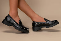 Black loafers with stud details worn by a person on a beige background