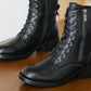 Pair of black leather boots with laces and a zipper on a wooden surface.