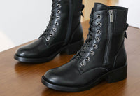 Pair of black leather boots with laces and a zipper on a wooden surface.
