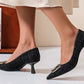 Black textured high heels worn by a person on a neutral background