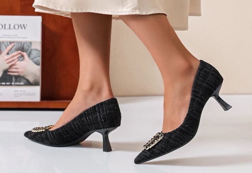 Black textured high heels worn by a person on a neutral background