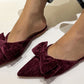 Brown velvet pointed flat shoe on a flat with a white background. With bow detail 
