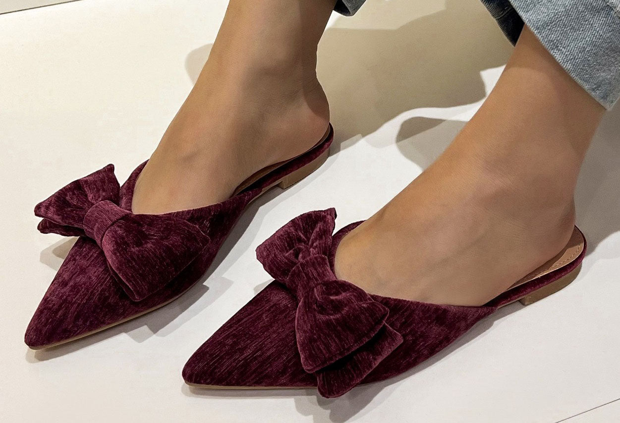 Brown velvet pointed flat shoe on a flat with a white background. With bow detail 