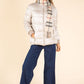Woman wearing a silver puffer jacket, blue pants, and a plaid scarf on a beige background