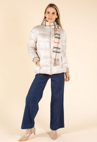 Woman wearing a silver puffer jacket, blue pants, and a plaid scarf on a beige background