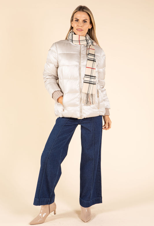Woman wearing a silver puffer jacket, blue pants, and a plaid scarf on a beige background
