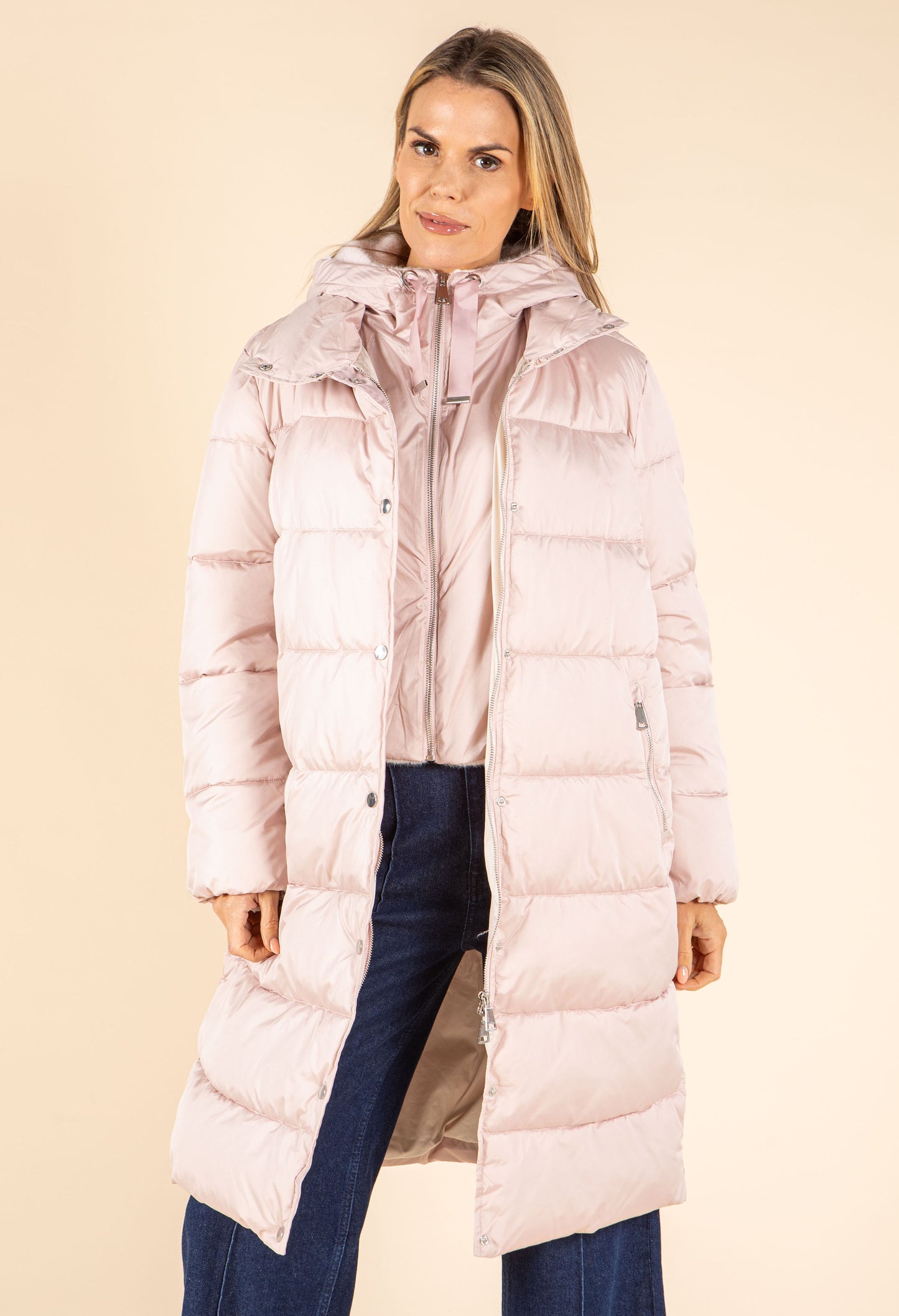 Woman wearing a long pink puffer coat against a beige background