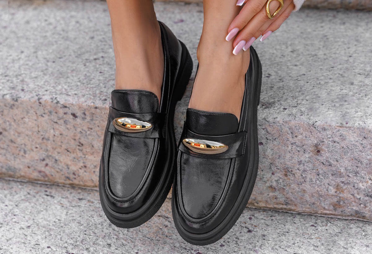 Black loafers with gold accents worn by a person on a stone surface