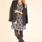 Woman wearing a floral dress with a black jacket and boots on a beige background