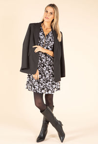 Woman wearing a floral dress with a black jacket and boots on a beige background