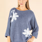 Woman wearing a blue sweater with white floral patterns on a beige background