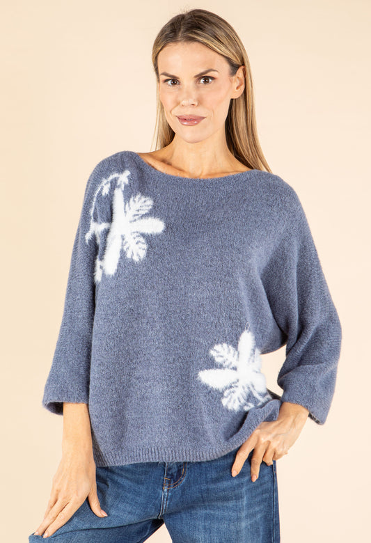 Woman wearing a blue sweater with white floral patterns on a beige background