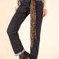 Person wearing dark blue jeans with a leopard print scarf tied around the waist on a beige background