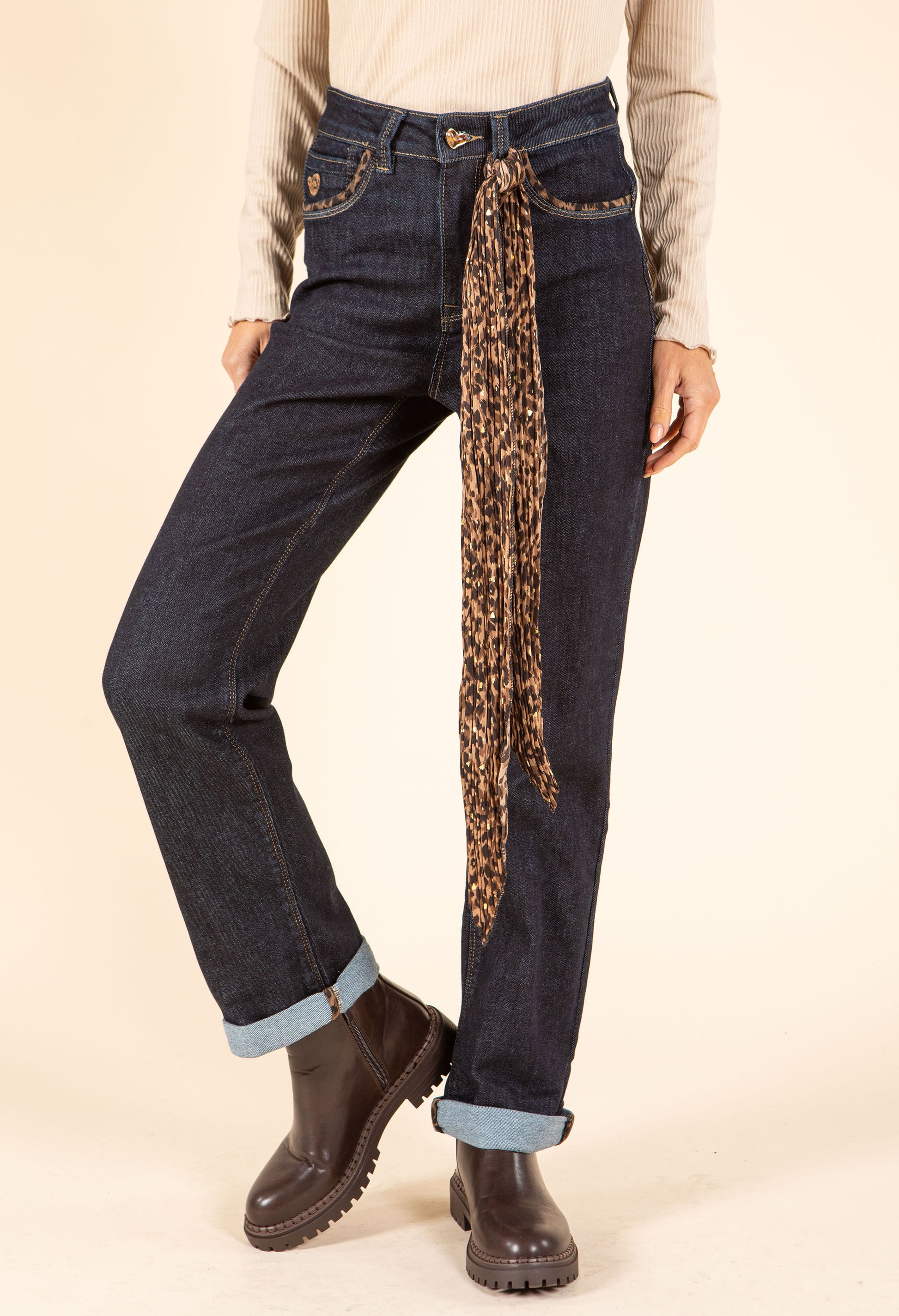 Person wearing dark blue jeans with a leopard print scarf tied around the waist on a beige background