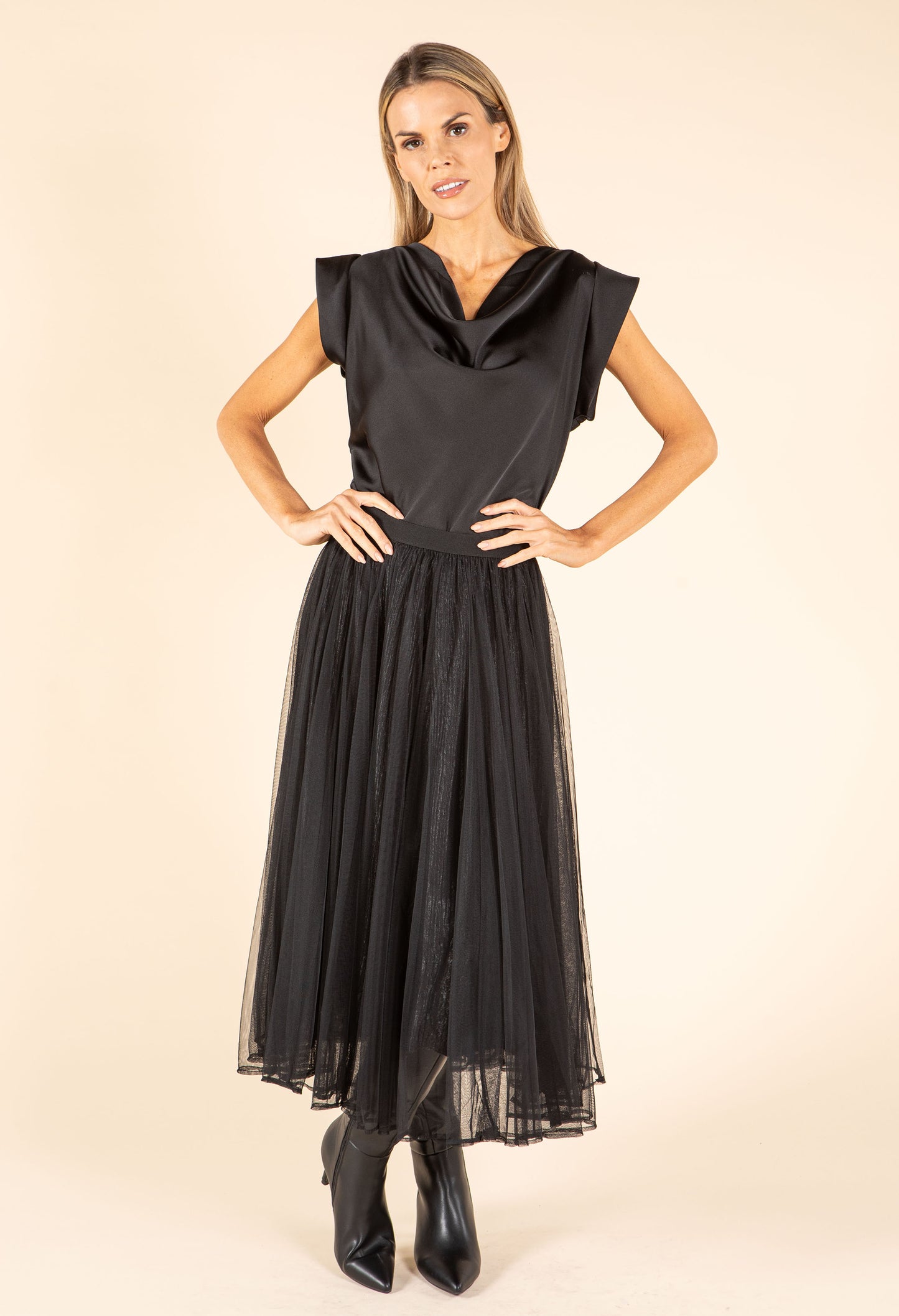 Woman wearing a black dress with a cowl neckline on a beige background